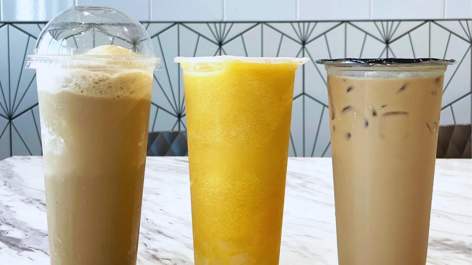 Three tea drinks including iced milk tea, mango slush with jelly, and classic boba sit on a marble cafe counter.