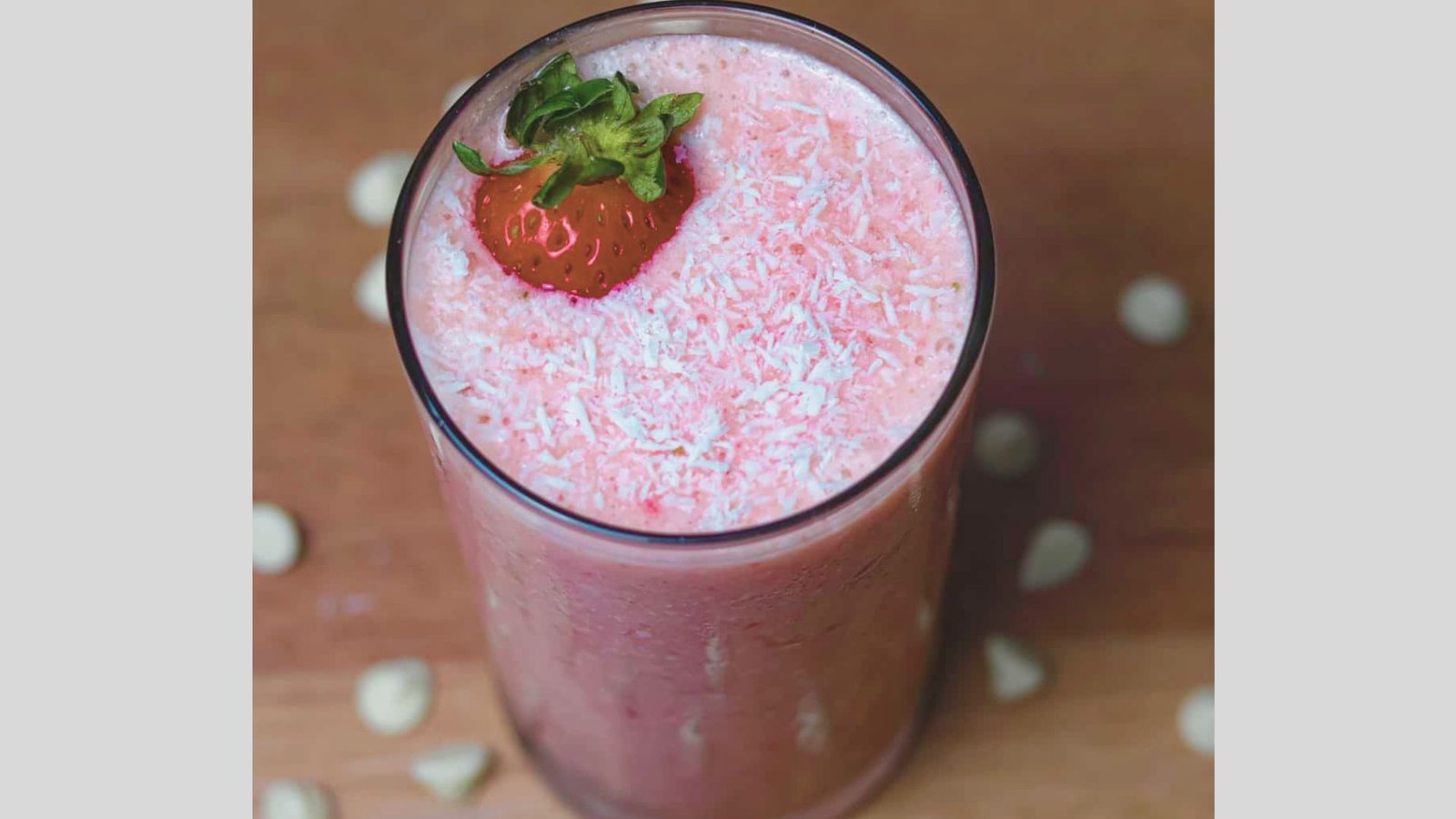 Top-down view of a creamy pink Bahama Mama Tropical Smoothie in a tall glass, topped with shredded coconut and a fresh strawberry.