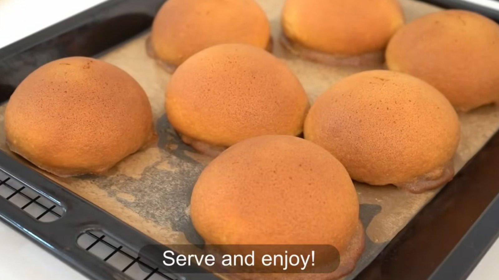 Seven golden-brown baked coffee buns fresh out of the oven on a parchment-lined baking tray with a "Serve and enjoy!" caption.