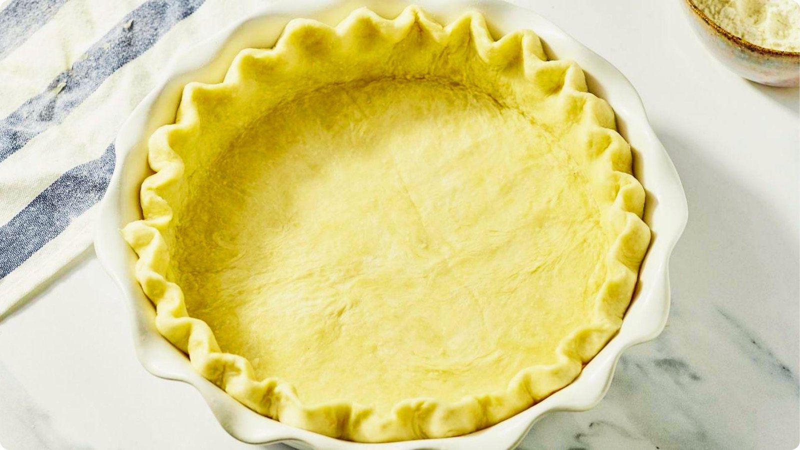Unbaked fluted pie crust pressed into a white ceramic pie dish.