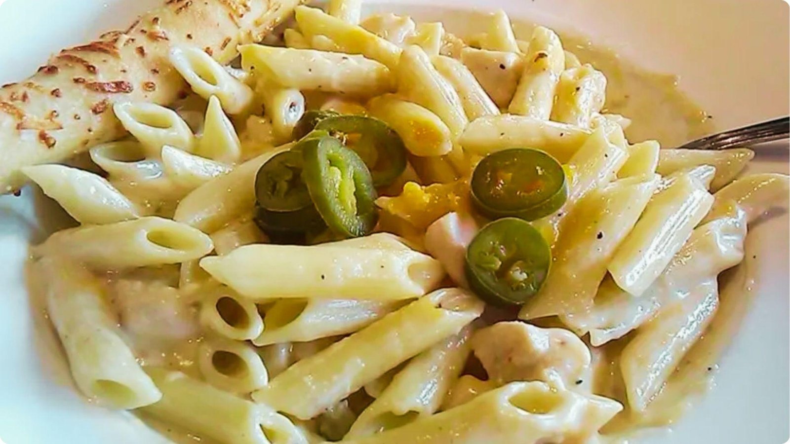 Bowl of creamy rattlesnake pasta with penne, chicken pieces, and sliced jalapeños in a rich white sauce.