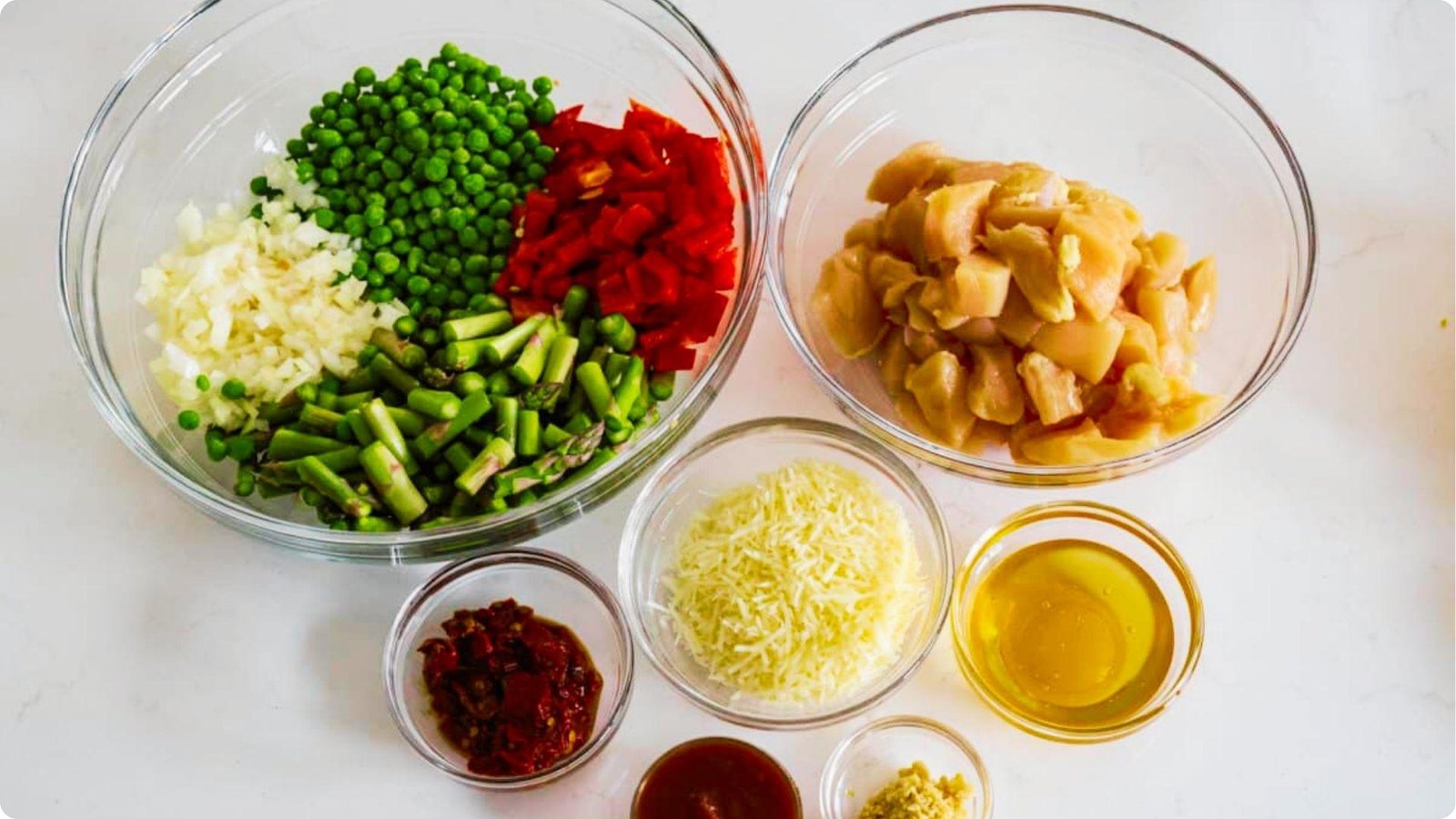 Top-down view of chipotle pasta ingredients prepped in glass bowls: diced chicken, veggies, and sauces.