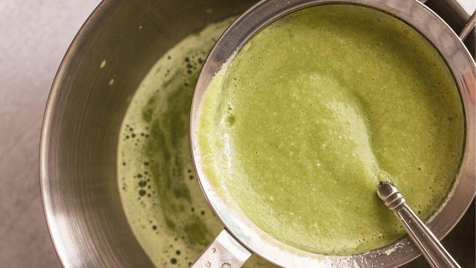 Blended cucumber mint agua fresca mixture strained through fine mesh sieve into stainless steel bowl