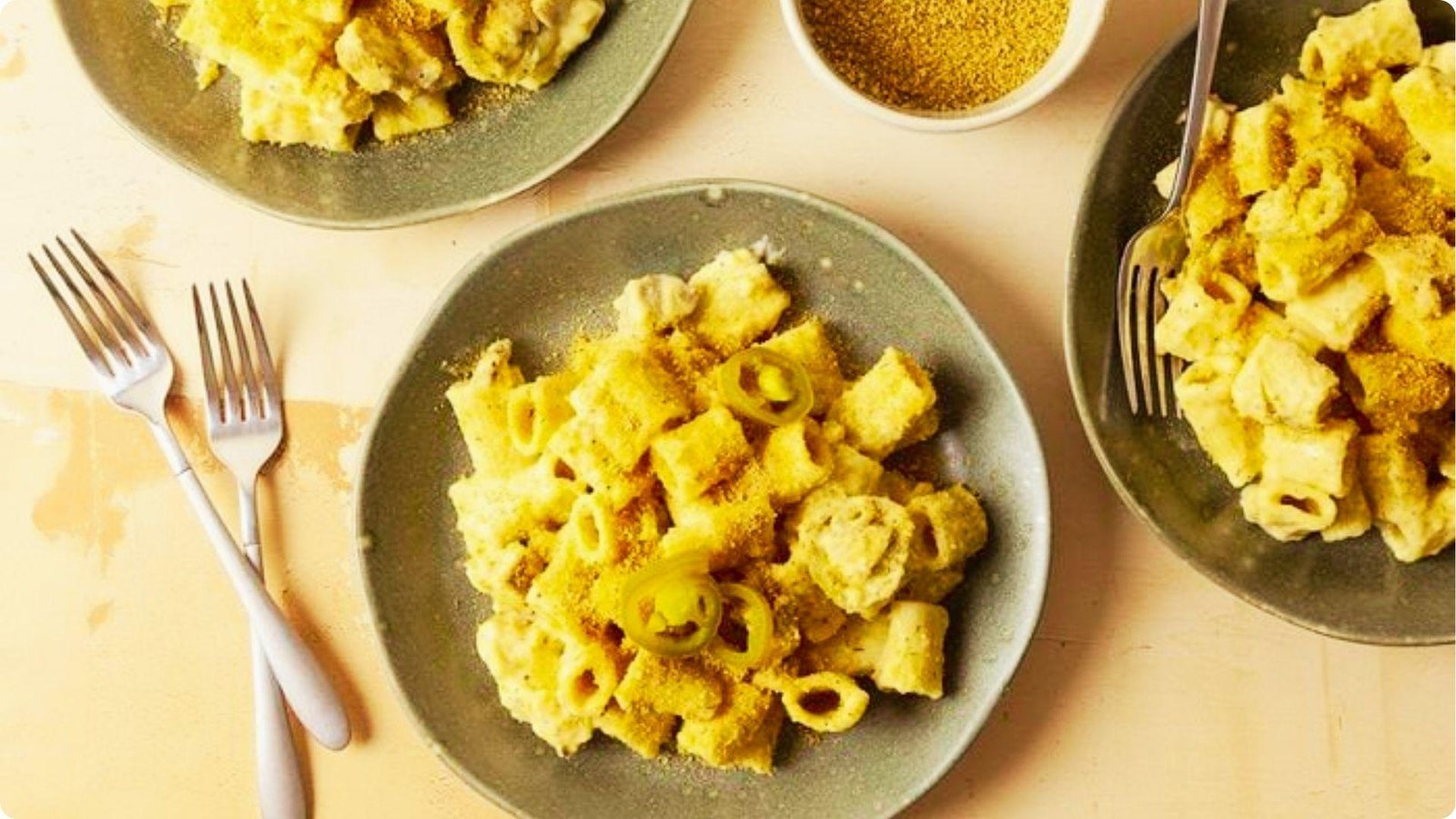 Overhead view of three plates of rattlesnake pasta with rigatoni, chicken, and sliced jalapeños in a golden cheese sauce.