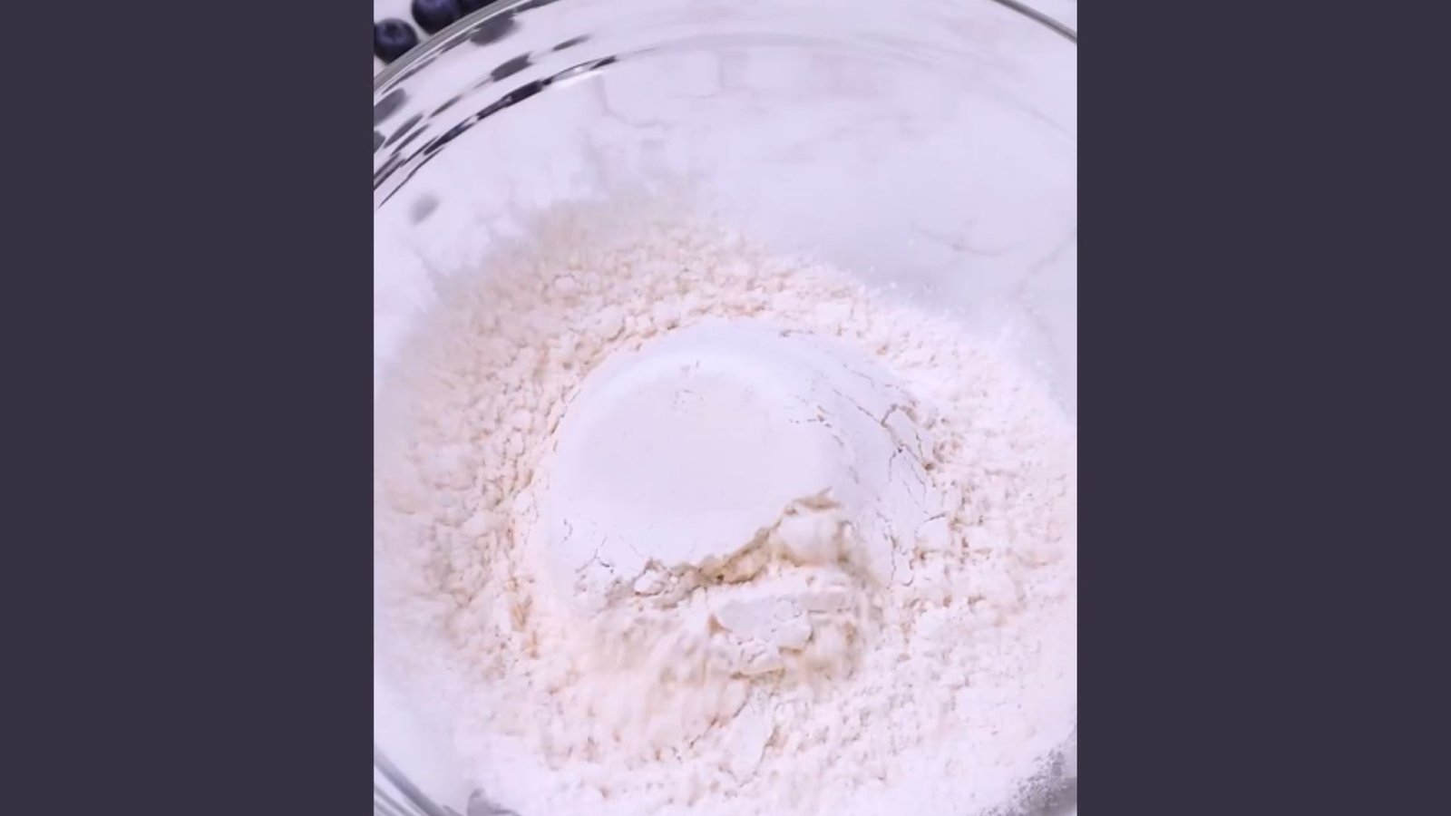 Close-up of white flour in clear glass mixing bowl as first step for blue waffle recipe