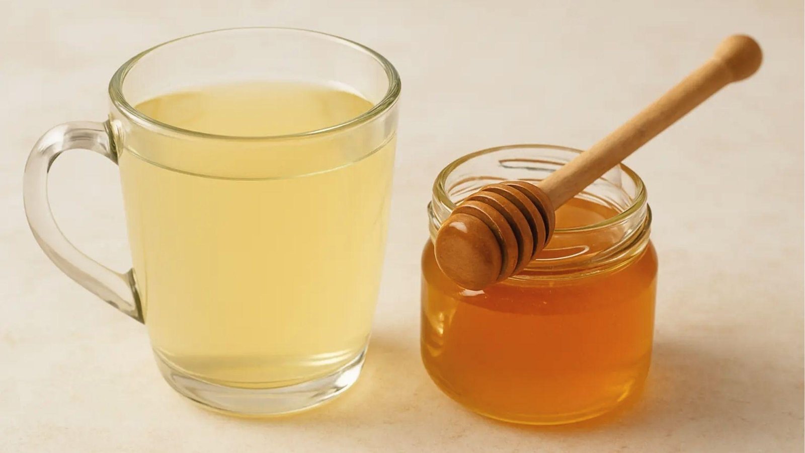 Glass mug of lemon water beside honey jar and dipper to make honey trick detox drink.
