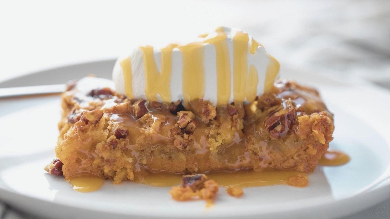 A slice of Pumpkin Crunch on a white plate, drizzled with caramel sauce over toasted pecans and a dollop of whipped cream.