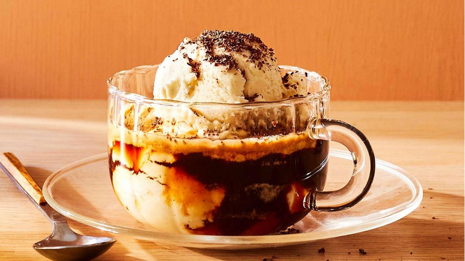 An affogato in a glass cup with a vanilla ice cream scoop topped with chocolate shavings over dark espresso.