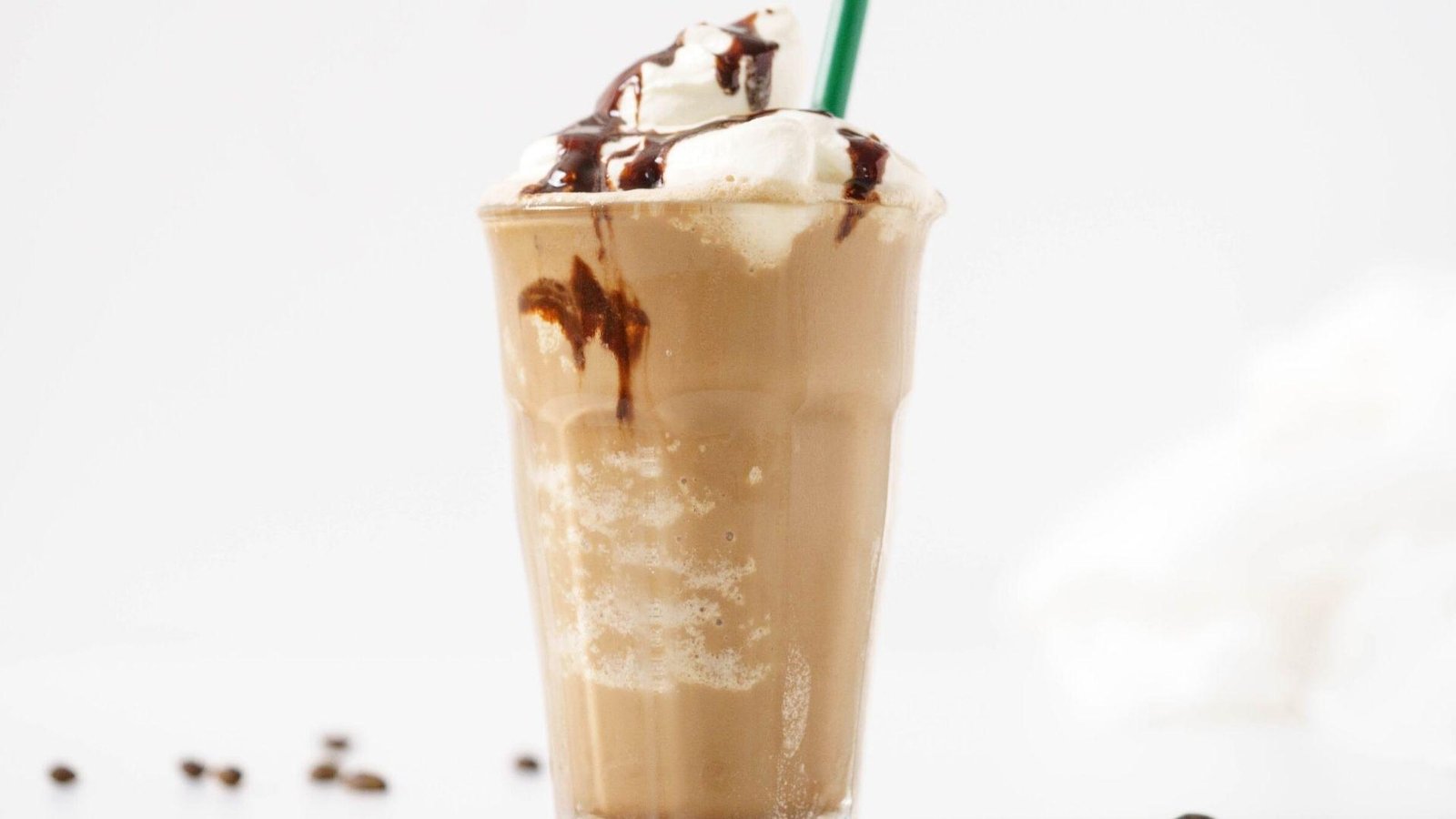 A blended mocha frappuccino in a clear cup topped with whipped cream and chocolate sauce drizzle with a green straw.