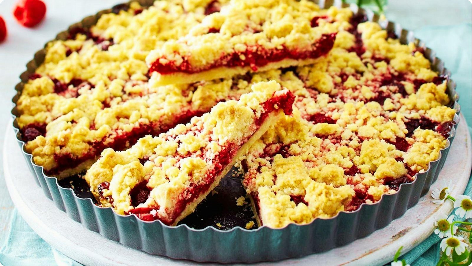 German raspberry Streuselkuchen baked in a fluted tart pan with golden crumble topping over red fruit filling.