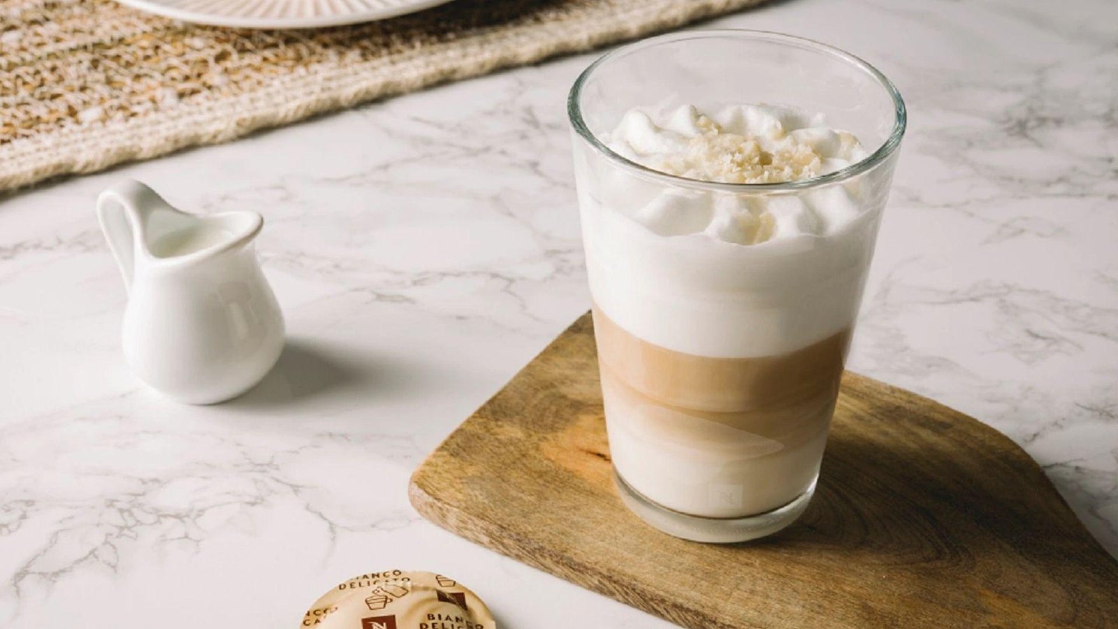 A tall glass of layered latte macchiato with a maple syrup jar kept besides it.