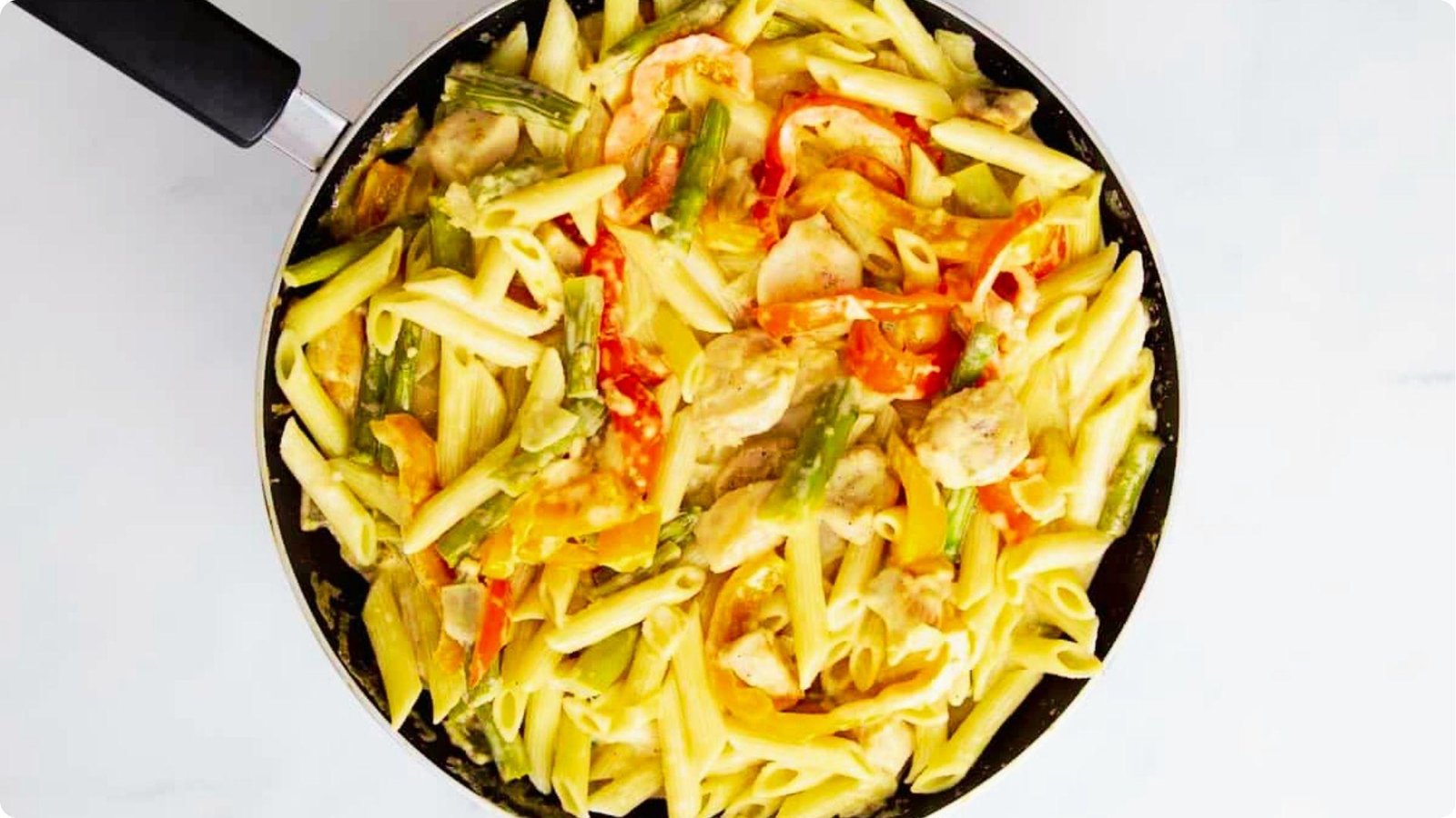 Overhead view of a skillet filled with chipotle chicken penne pasta, asparagus, and red bell peppers.