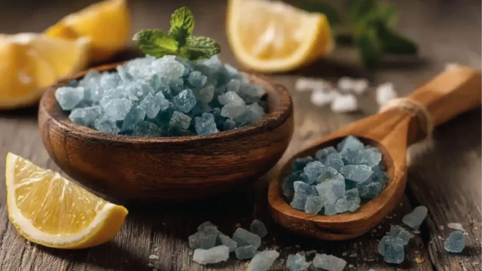 Blue salt crystals in wooden bowl and spoon with mint and lemon wedges for blue salt trick drink