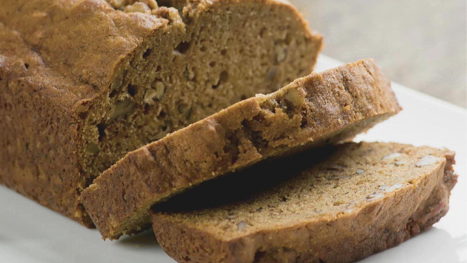 Sliced coffee walnut bread with a tender crumb and visible nut pieces on a white plate.