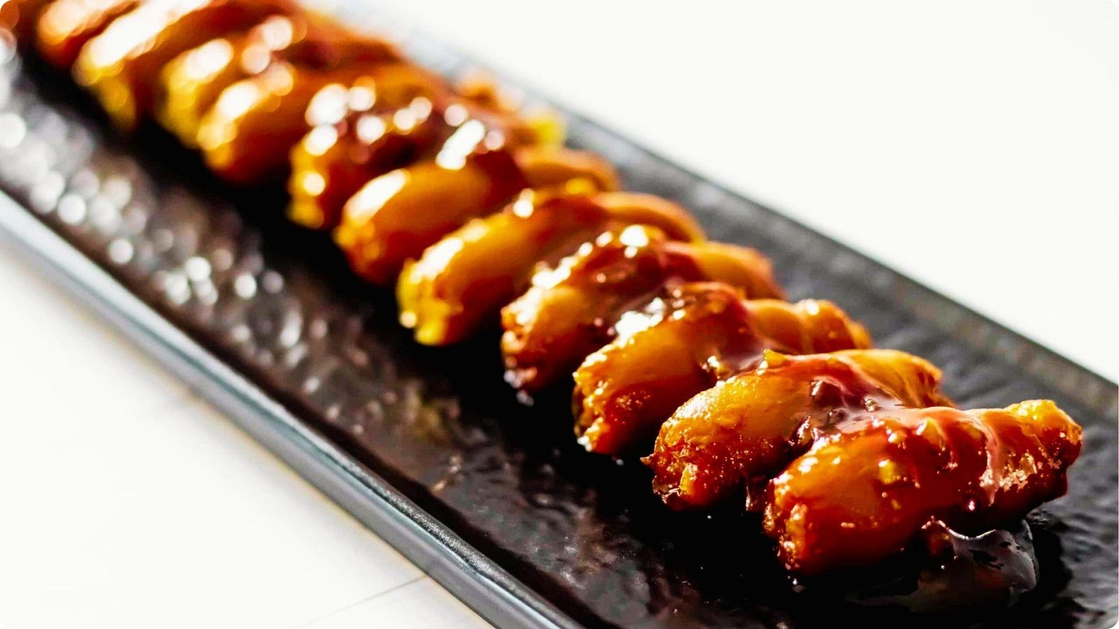 Glazed chicken or pork pieces lined up on a dark rectangular plate, coated in a shiny honey garlic sauce.