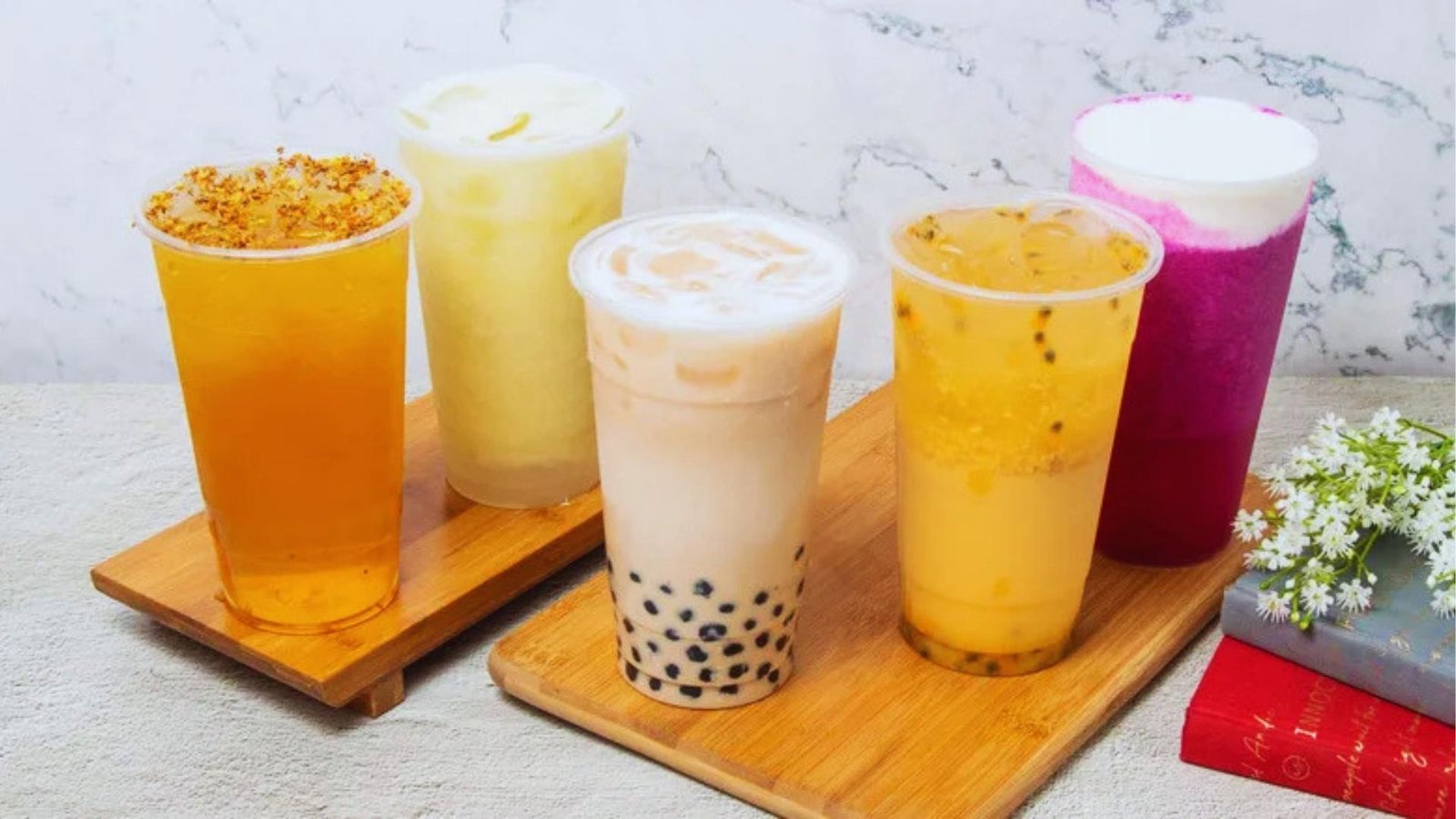 Five colorful bubble tea drinks including milk tea with boba, passion fruit, and pink dragon fruit arranged on bamboo trays.