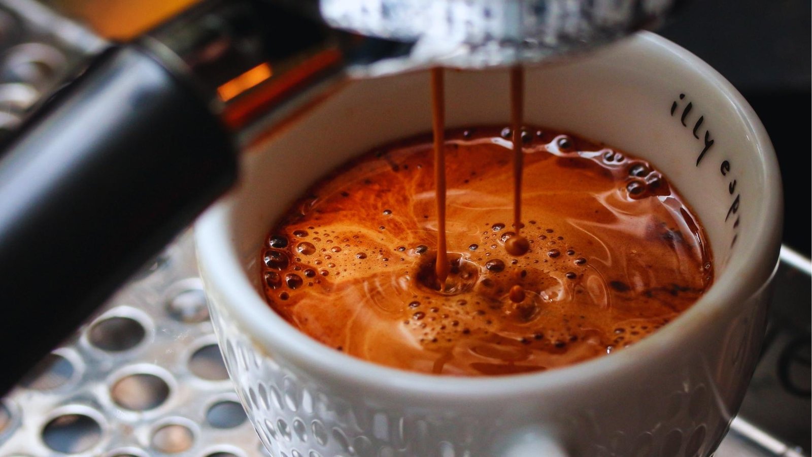 Close-up of espresso shot pouring into an illy cup, capturing golden crema and dark streams from espresso machine portafilter.