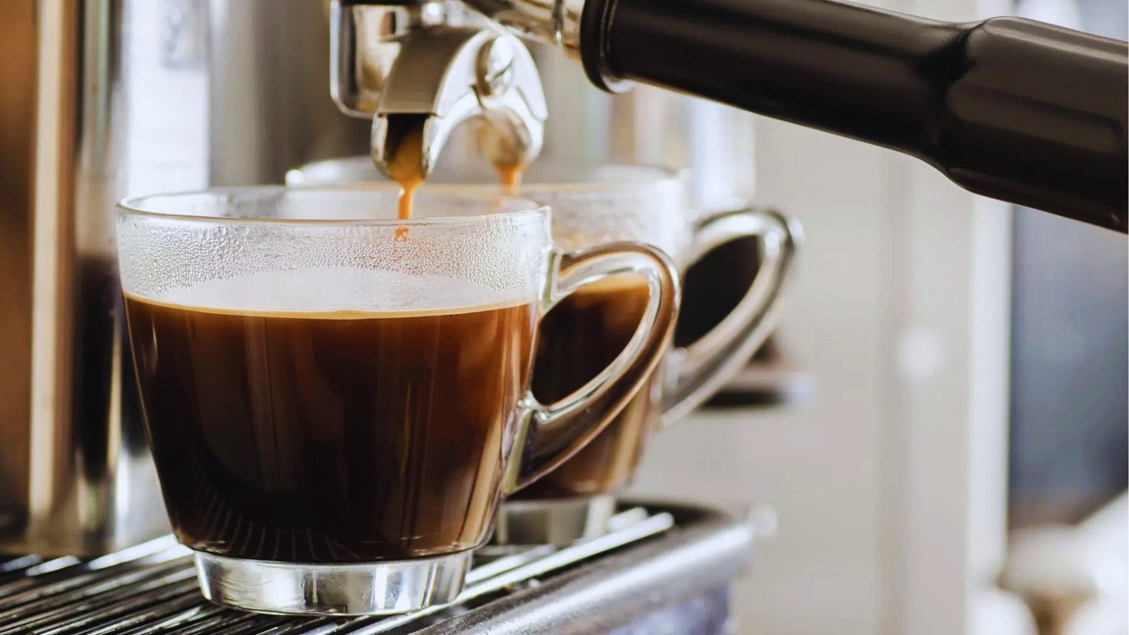 Espresso streams from portafilter into two clear glass mugs, forming rich crema on top of dark Americano coffee.