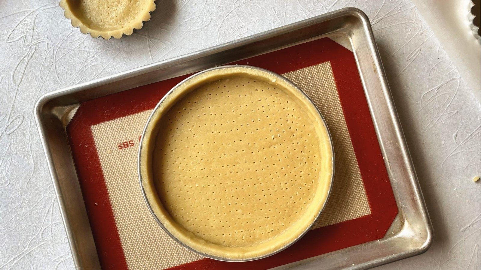 Raw pate sablee tart shell docked with fork in ring on baking mat, set for blind baking