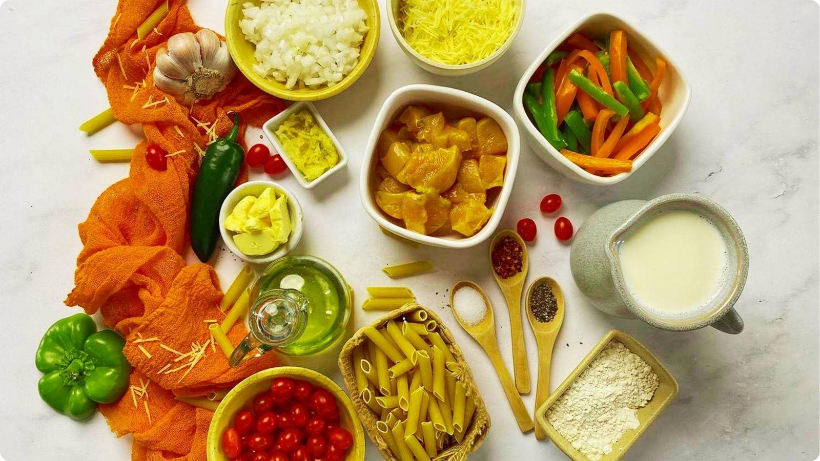 Flat lay of rattlesnake pasta ingredients on a white surface including uncooked penne, diced chicken, sliced peppers, and cherry tomatoes.
