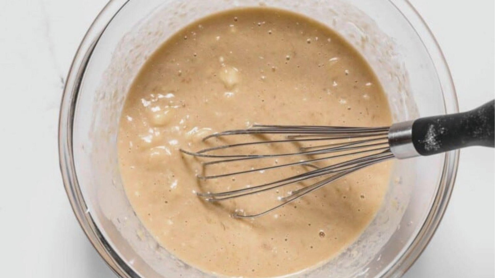 Overhead shot of light brown coffee bread batter being whisked in a clear glass bowl.