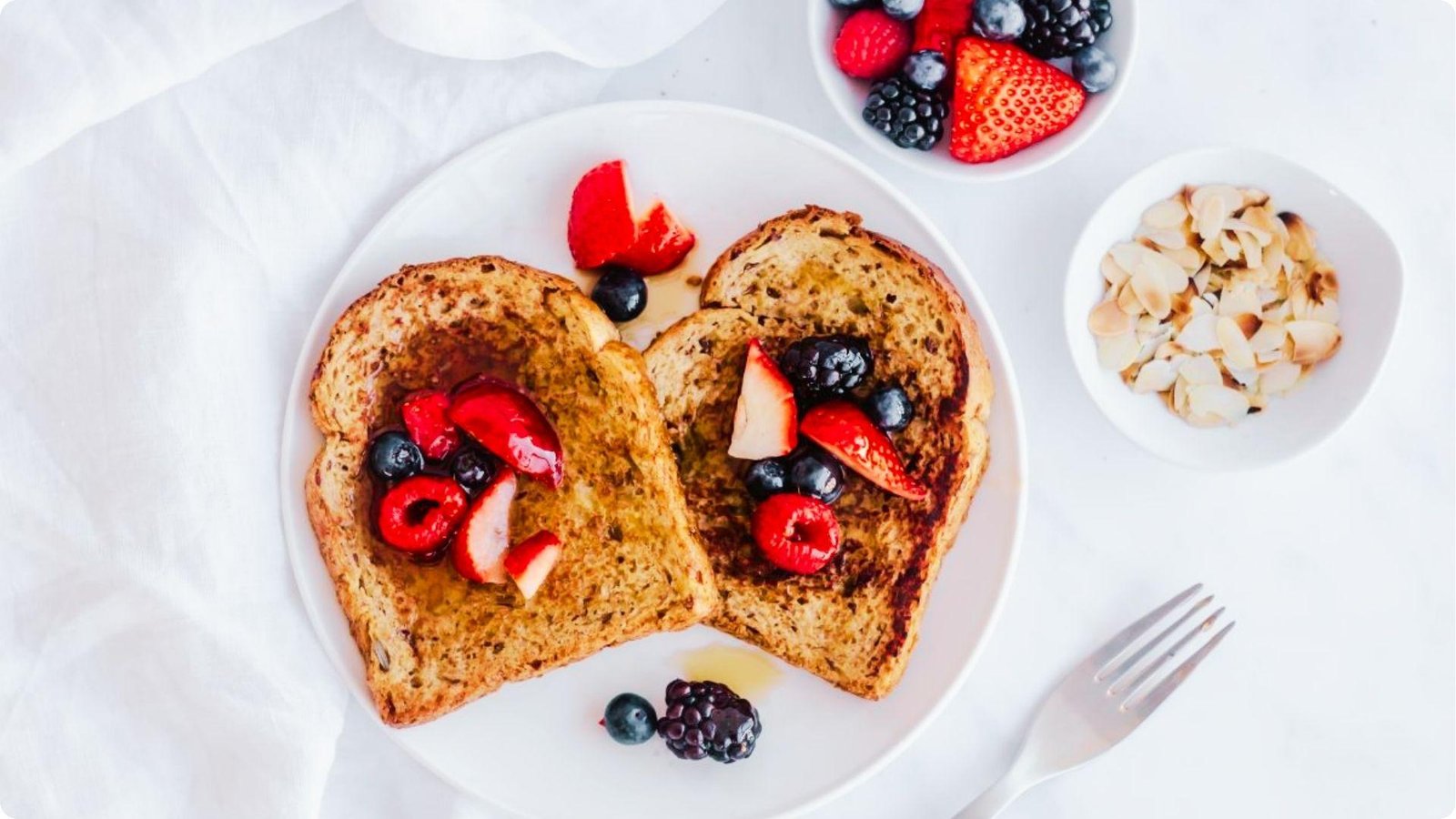 Two slices of golden-brown wheat bread French toast topped with fresh strawberries, blueberries, and raspberries.