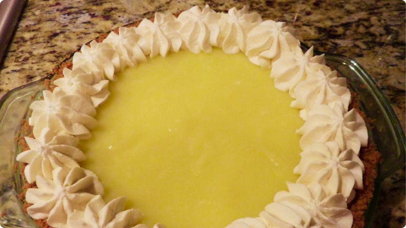 Sour cream lemon pie in a glass dish with a graham cracker crust and piped whipped cream edge.