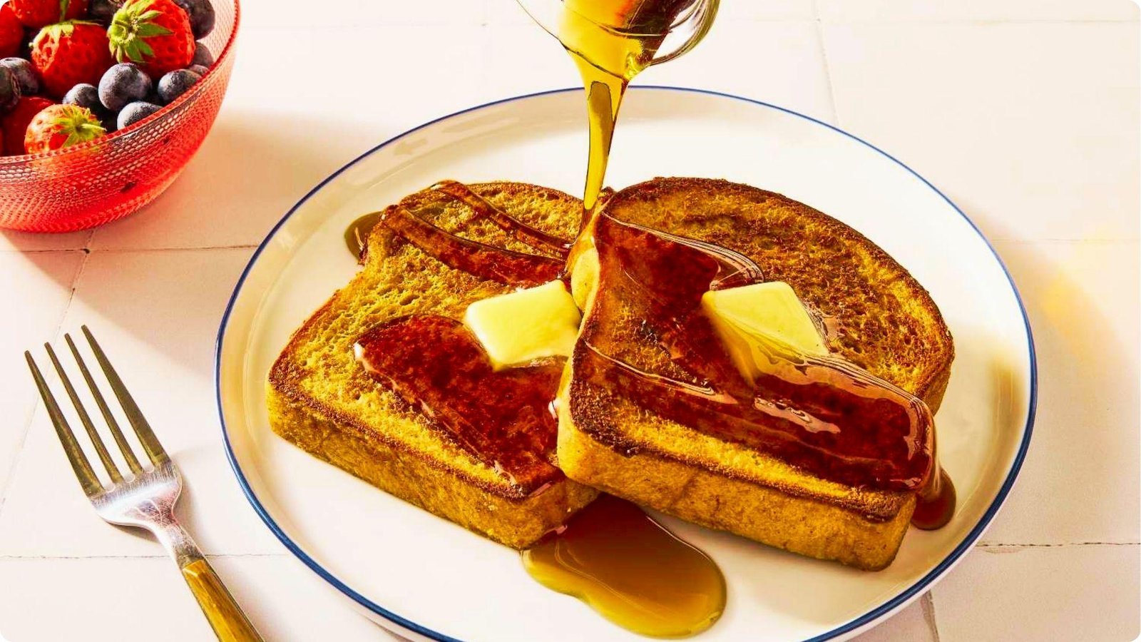 Two slices of wheat bread French toast on a white plate as maple syrup is poured over melting butter pats.