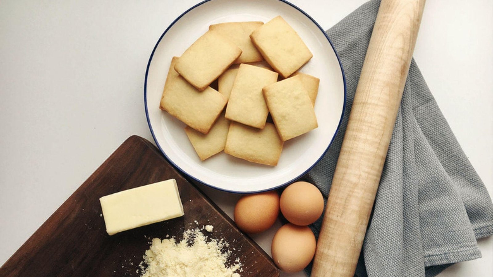 Baked pate sablee cookies on white plate with butter, eggs, flour and rolling pin beside