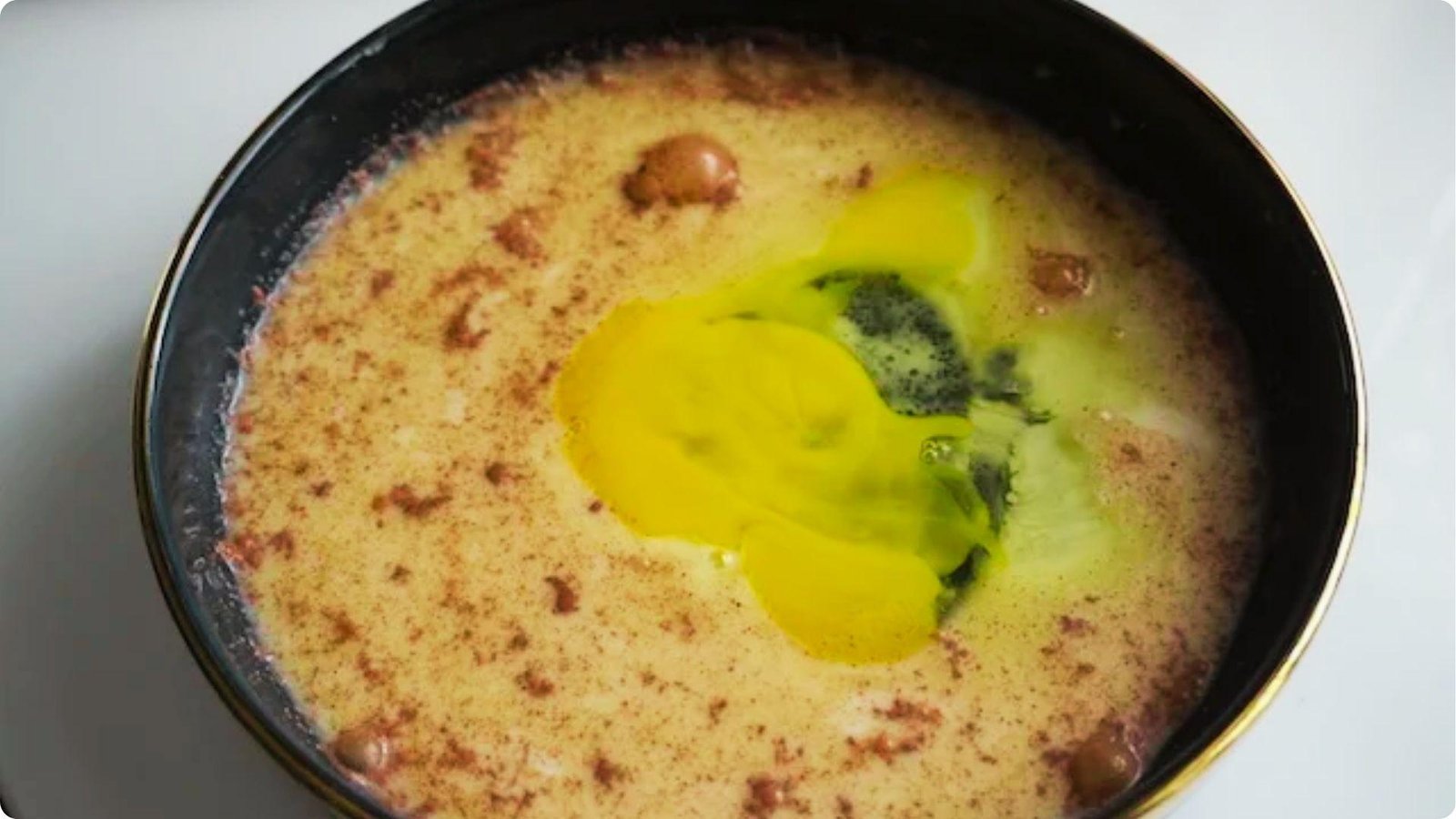 Overhead view of French toast batter in a black bowl with cracked eggs, milk, and cinnamon.
