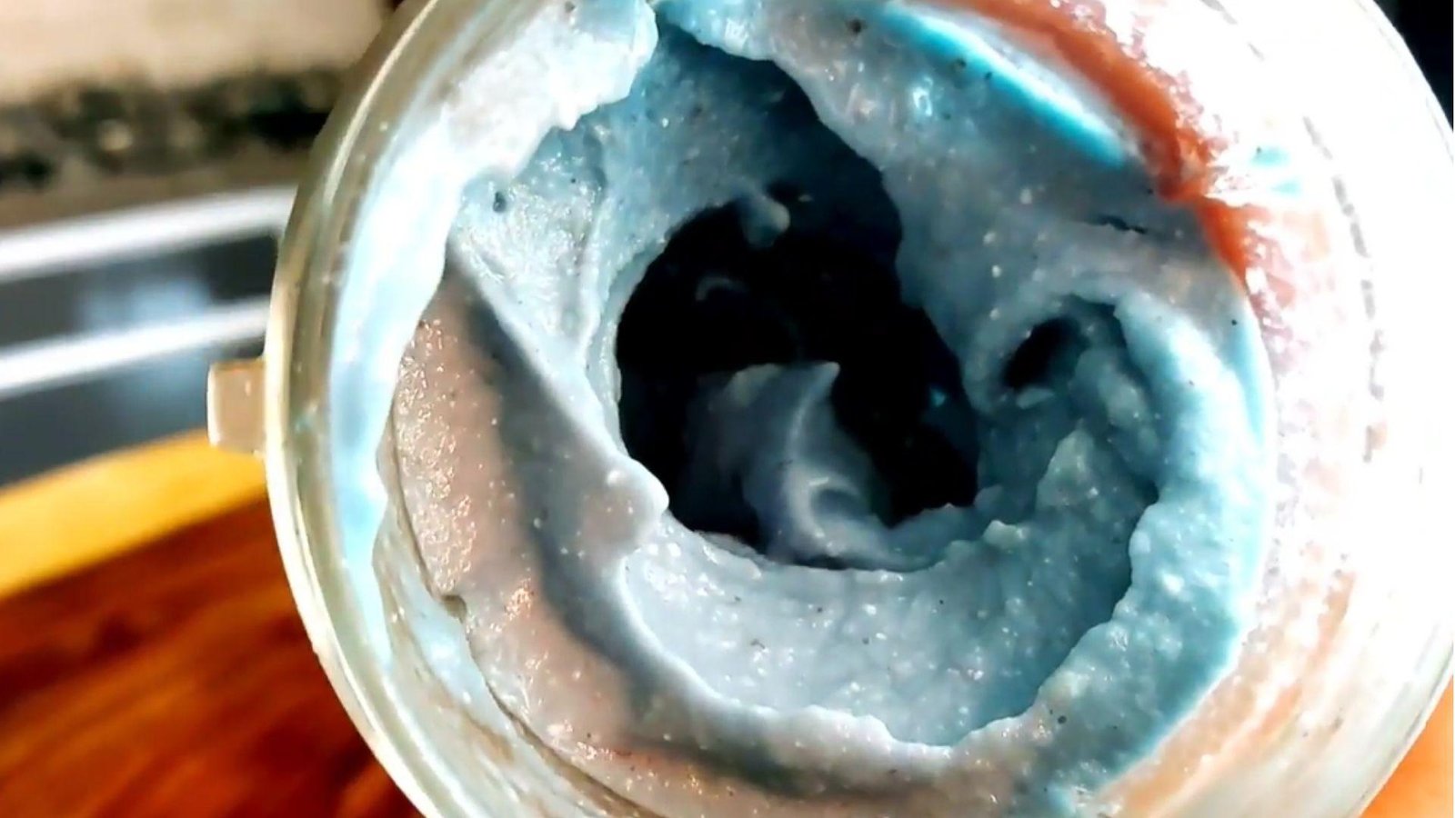 Overhead close-up of a vivid swirling blue spirulina smoothie mixture inside a blender cup after blending.