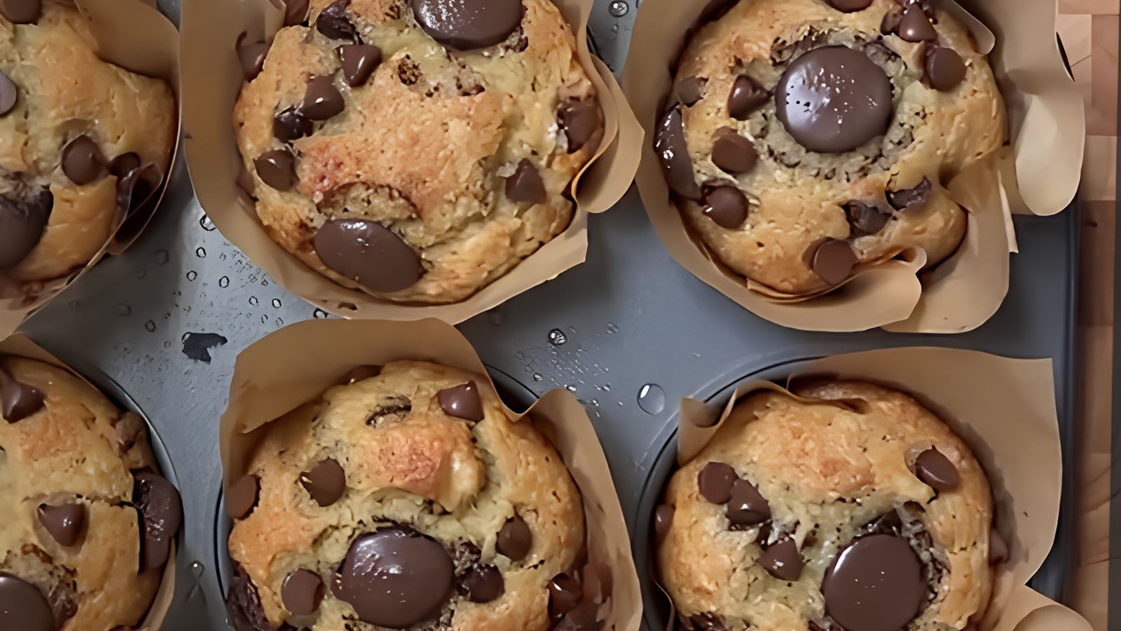 Top view of freshly baked banana chocolate chip muffins in parchment liners cooling in a metal muffin tray