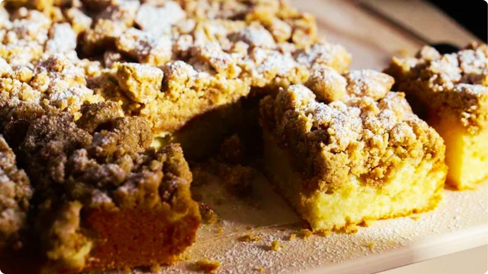 Close-up of German coffee cake squares with thick, chunky streusel crumbs dusted in powdered sugar.