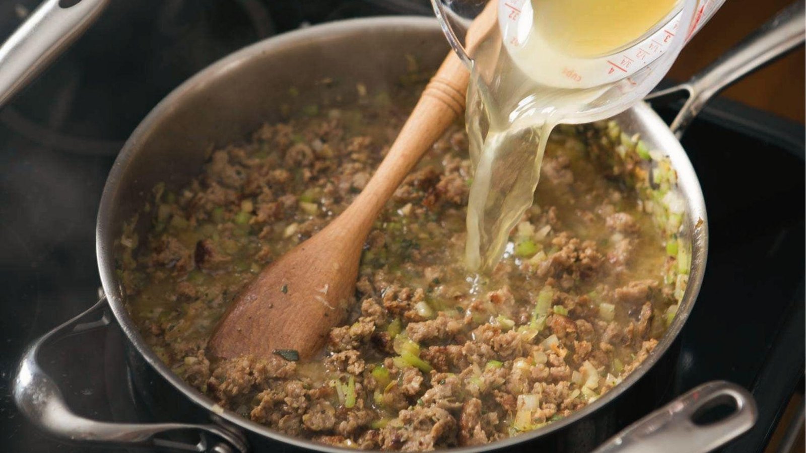 Pouring broth into skillet of browned sausage, onions, and celery for cornbread dressing base