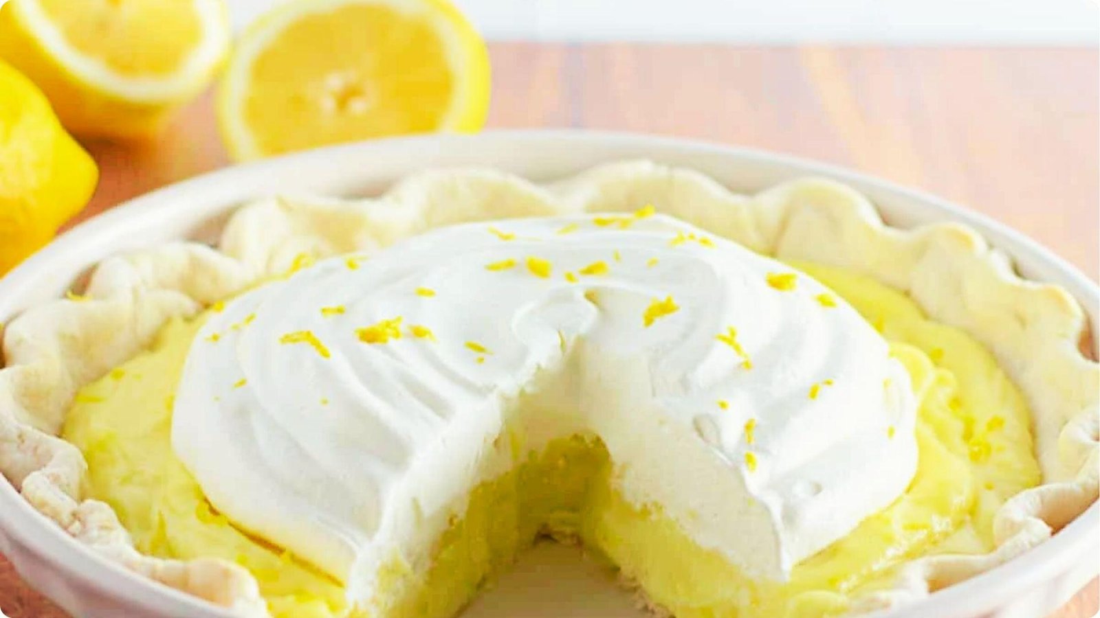 Close-up of a sliced sour cream lemon pie with fluffy whipped topping and lemon zest.