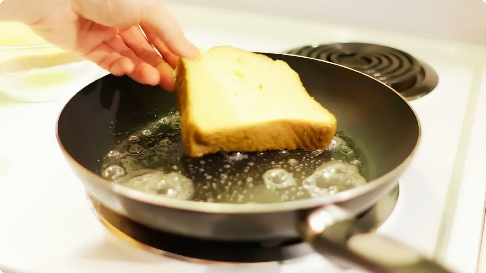 A hand places a custard-dipped slice of wheat bread into a hot, buttered frying pan.