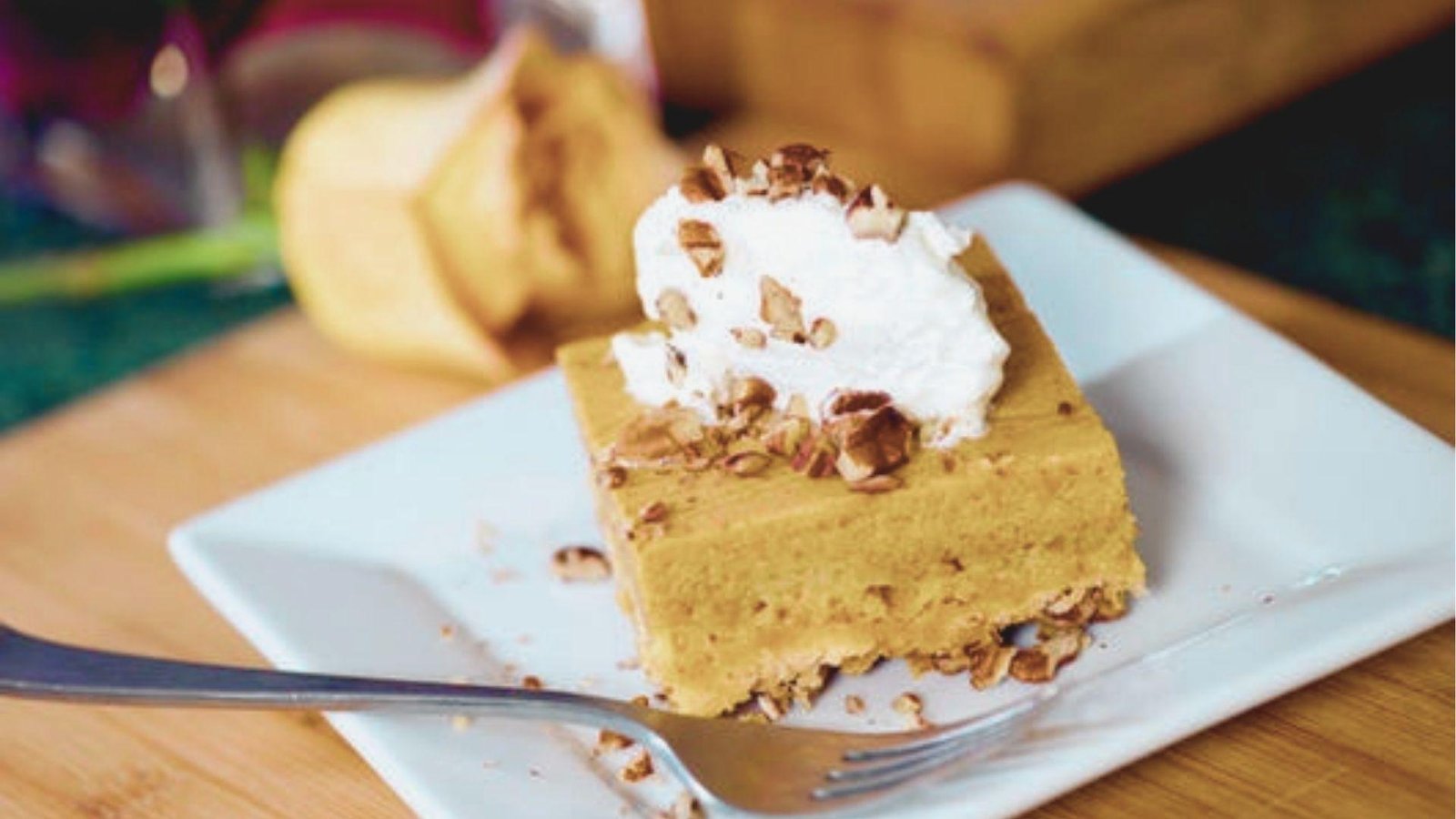 A slice of Pumpkin Crunch served on a square white plate with a fork, topped with whipped cream and chopped pecans.