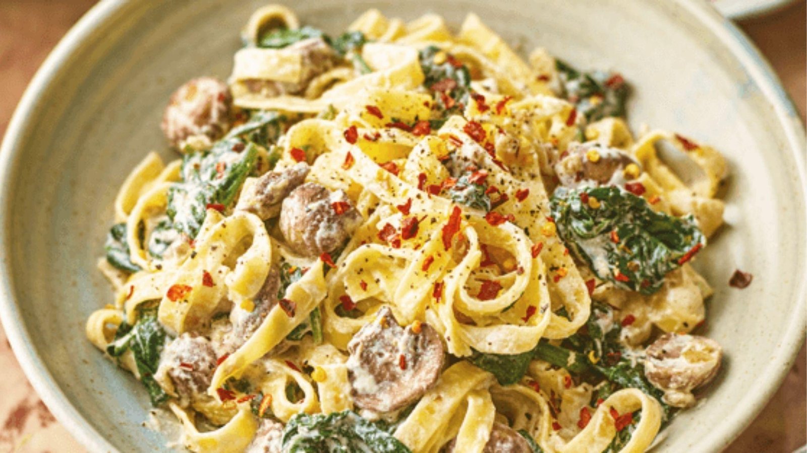 Creamy fettuccine pasta with mushrooms and spinach tossed in rich white sauce in ceramic bowl