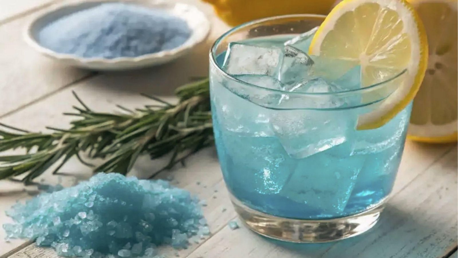 Iced blue salt trick recipe in short glass with lemon slice, blue salt crystals and rosemary sprigs
