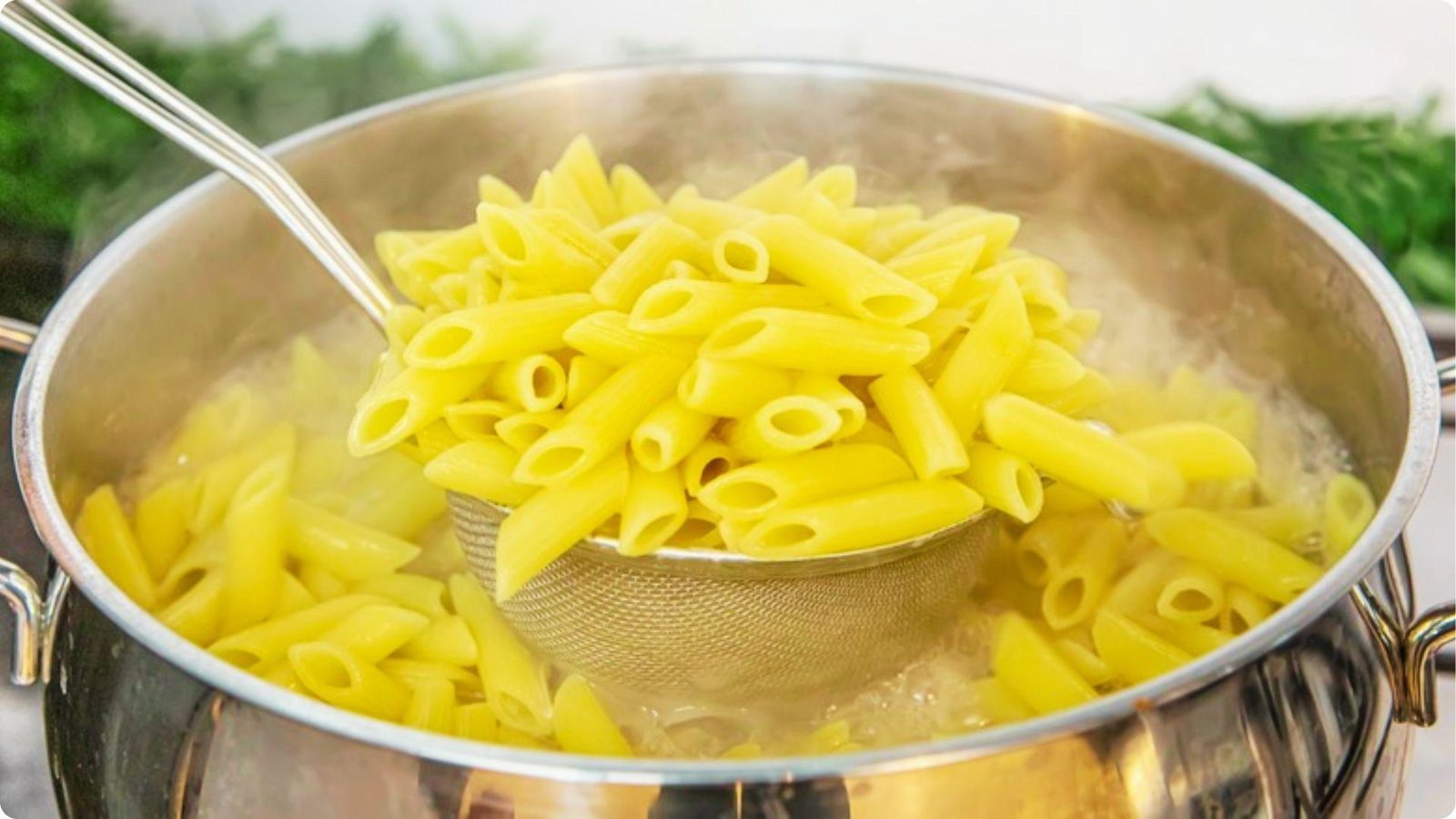 Steaming pasta being lifted from a pot of boiling water with a metal strainer.