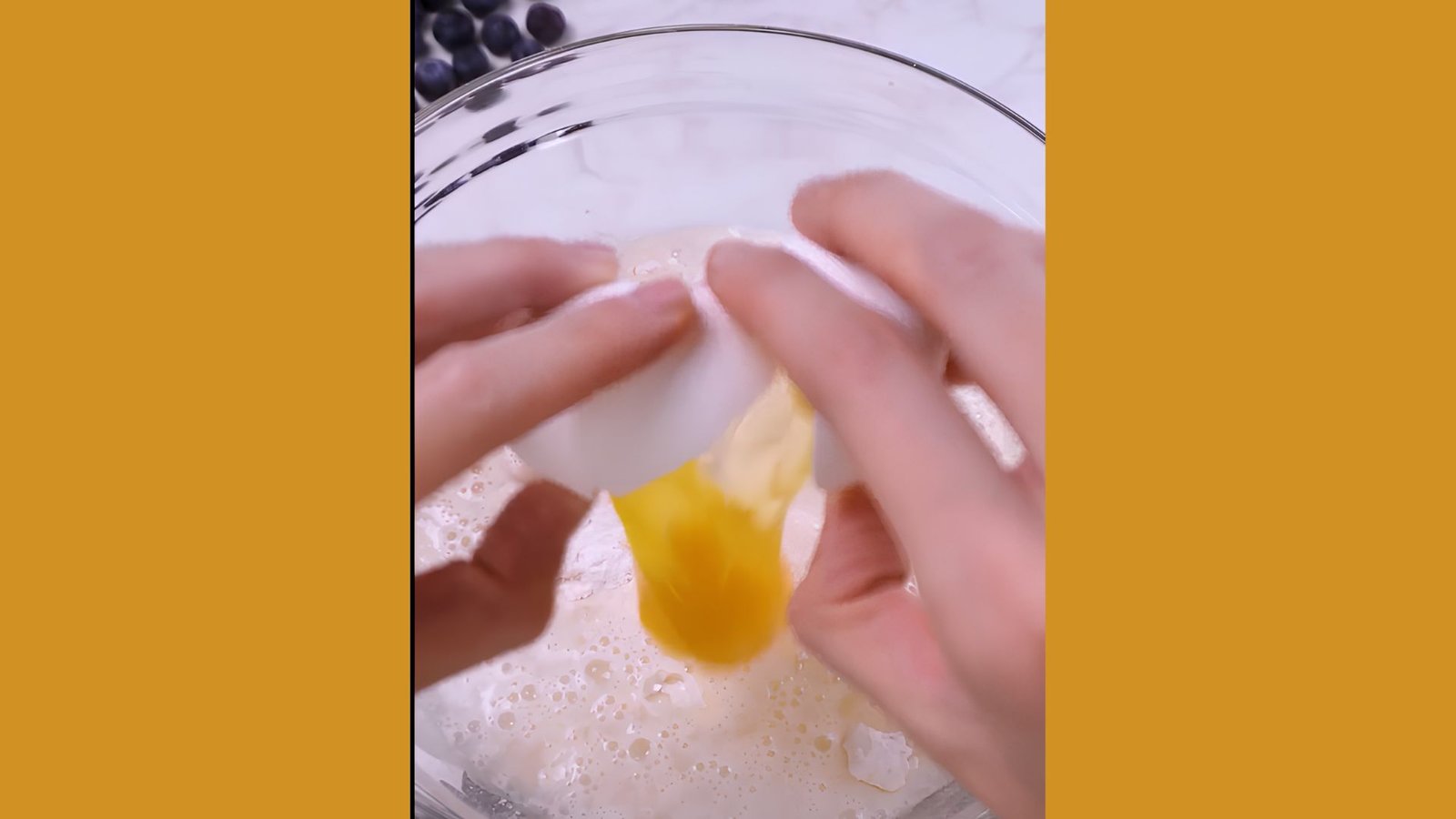 Hands cracking egg into waffle batter mixture with flour and liquid in clear glass mixing bowl