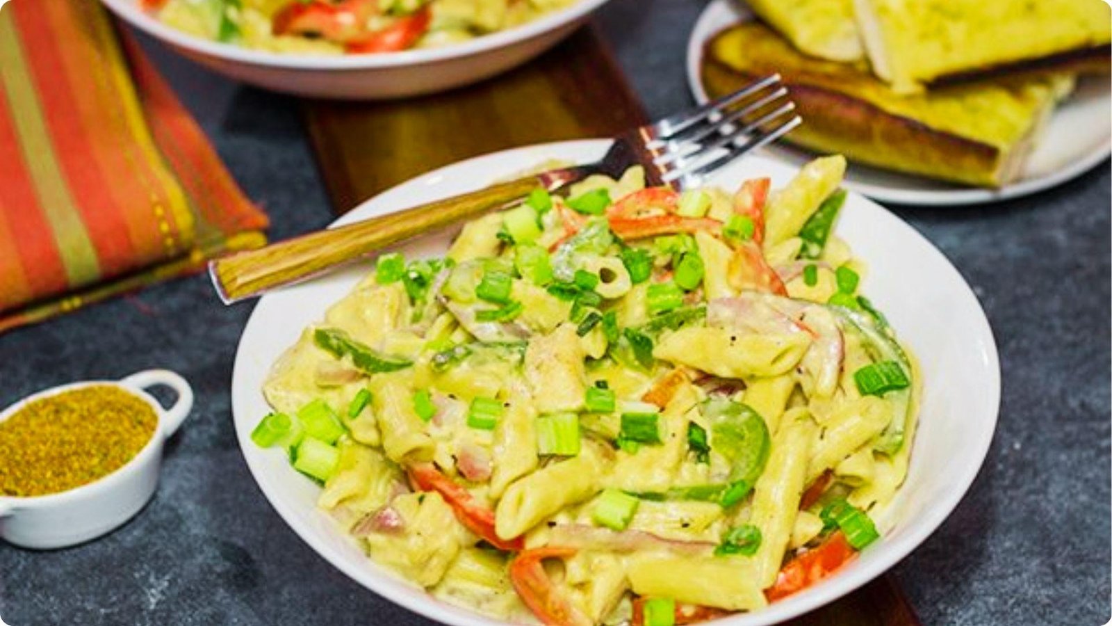 Creamy rattlesnake pasta with penne, red and green bell peppers, and green onions served in a white bowl.