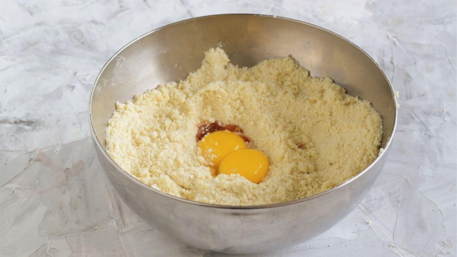 Adding egg yolks to crumbly flour mix to bind pate sablee dough ingredients