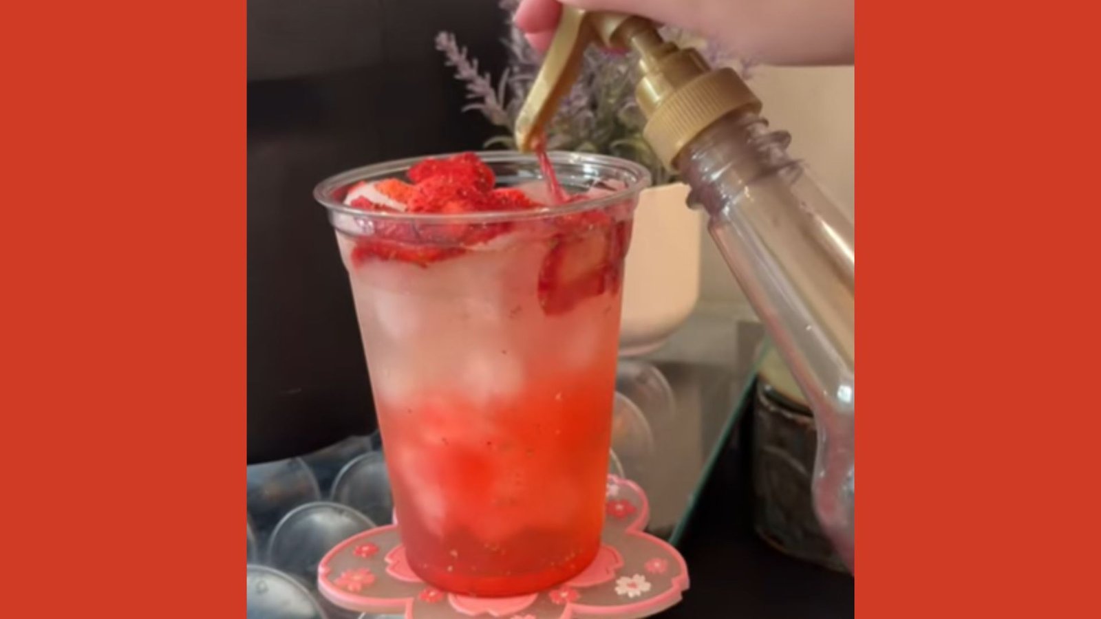 A hand using a gold pump dispenser to add syrup into a strawberry iced drink topped with freeze-dried strawberries.