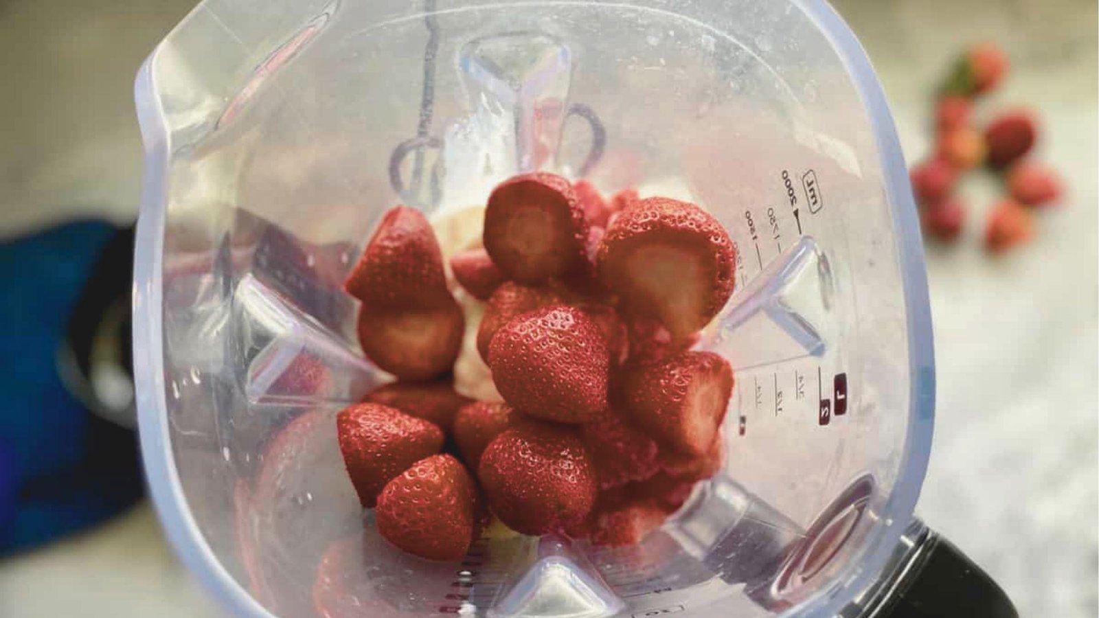 Overhead shot of fresh halved strawberries in a blender before blending.