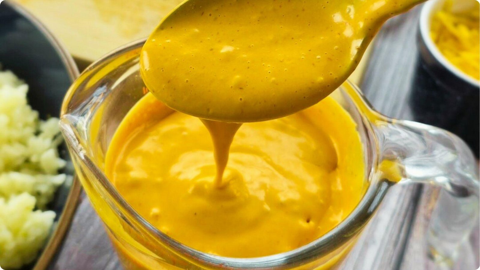 Thick, creamy orange chipotle sauce dripping from a spoon into a glass measuring cup.
