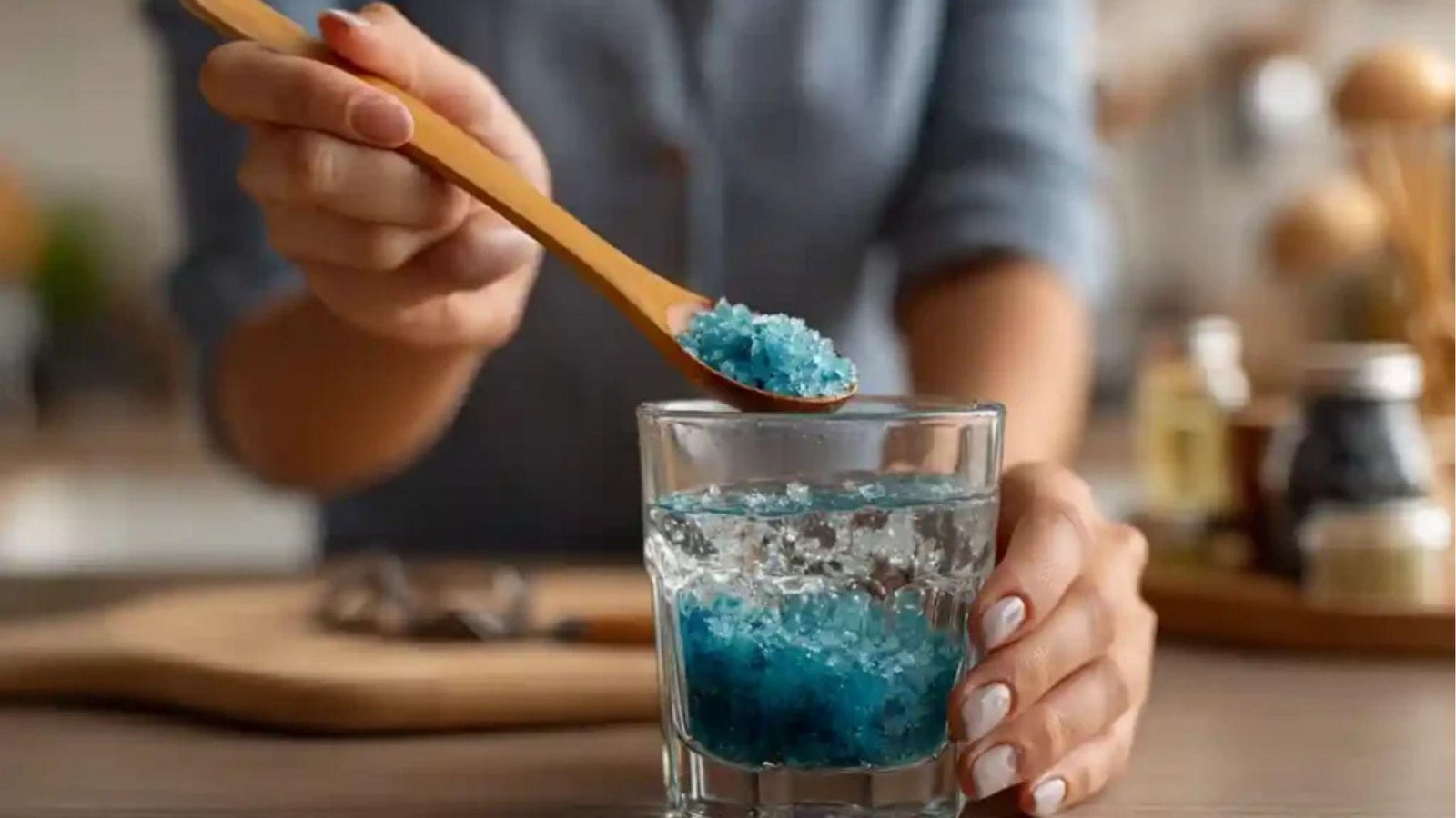 Person adding blue salt crystals from wooden spoon into glass of water for blue salt trick recipe