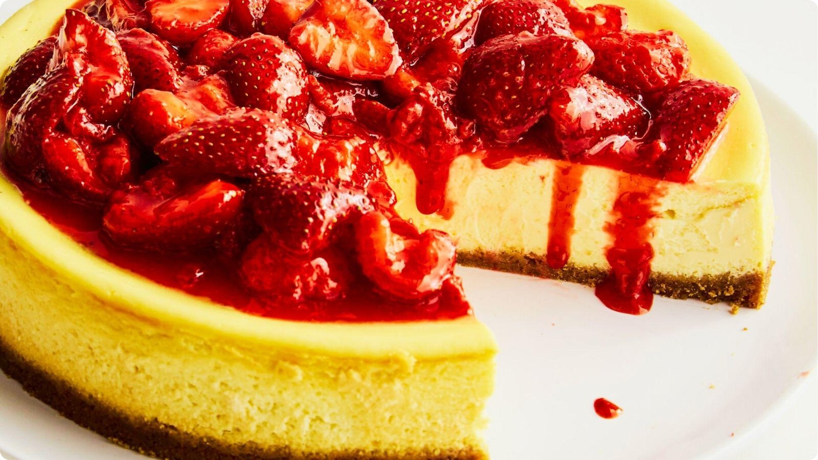 Close-up of a 6-inch cheesecake piled high with glossy strawberries and thick red strawberry sauce dripping down the sides.