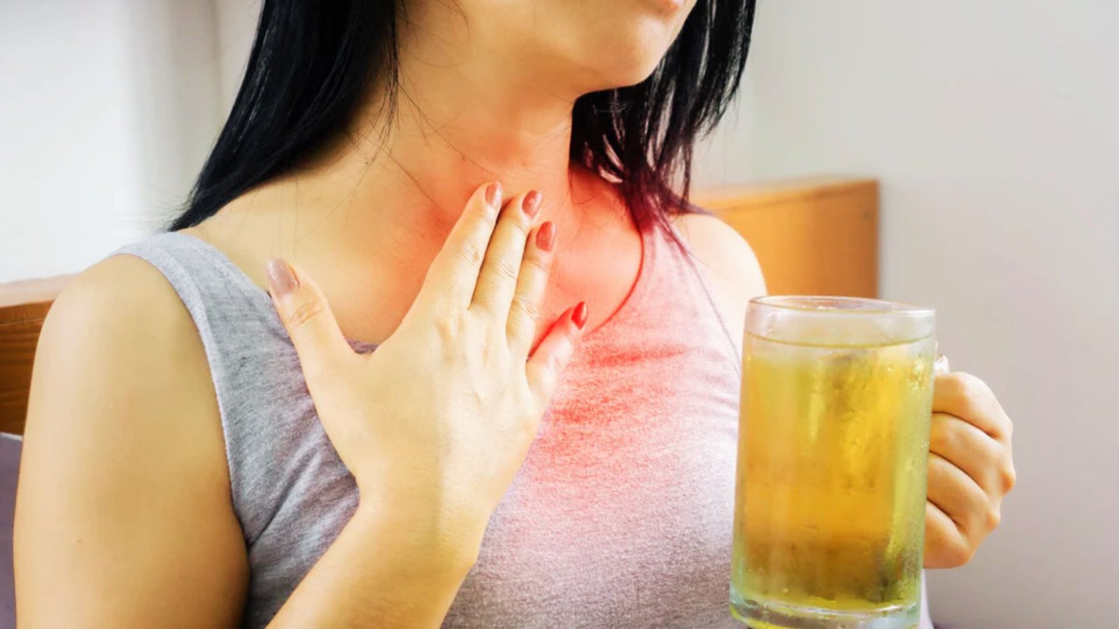 Woman touching red highlighted throat area while holding glass of kombucha, showing acid reflux symptoms.