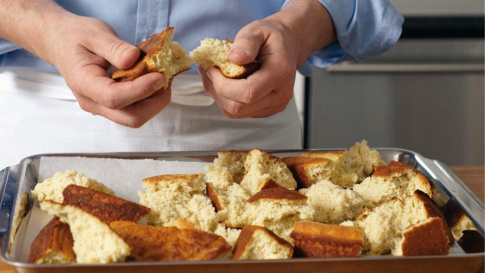 Hands tearing fresh cornbread into chunks over tray for homemade cornbread dressing recipe